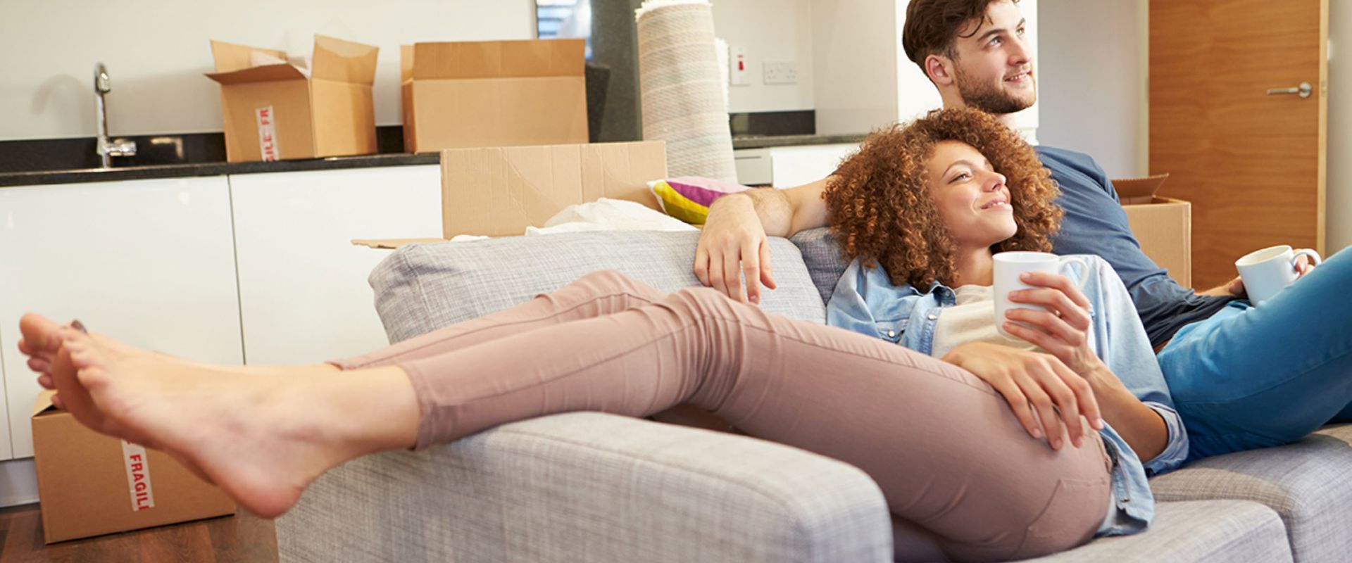 Young Couple On Grey Sofa Kitchen Boxes